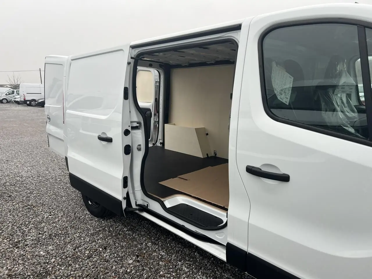 Vue latérale droite d’un utilitaire Nissan Primastar blanc 2025 avec porte coulissante ouverte montrant l’aménagement intérieur bois du Pack Cargo.