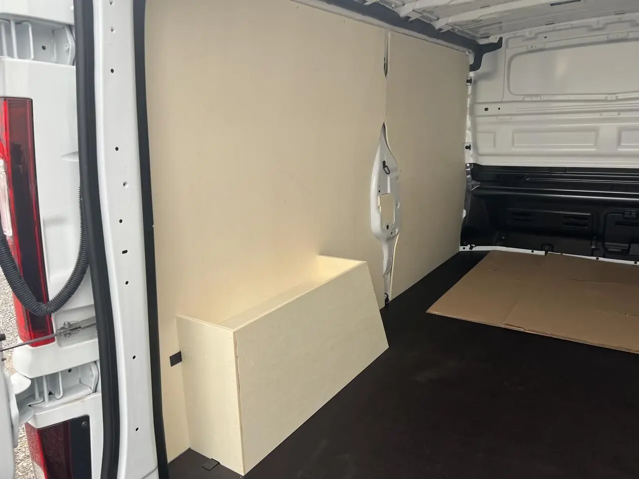 Vue intérieure arrière du Nissan Primastar blanc 2025, montrant le revêtement bois clair du coffre et des parois du compartiment cargo.