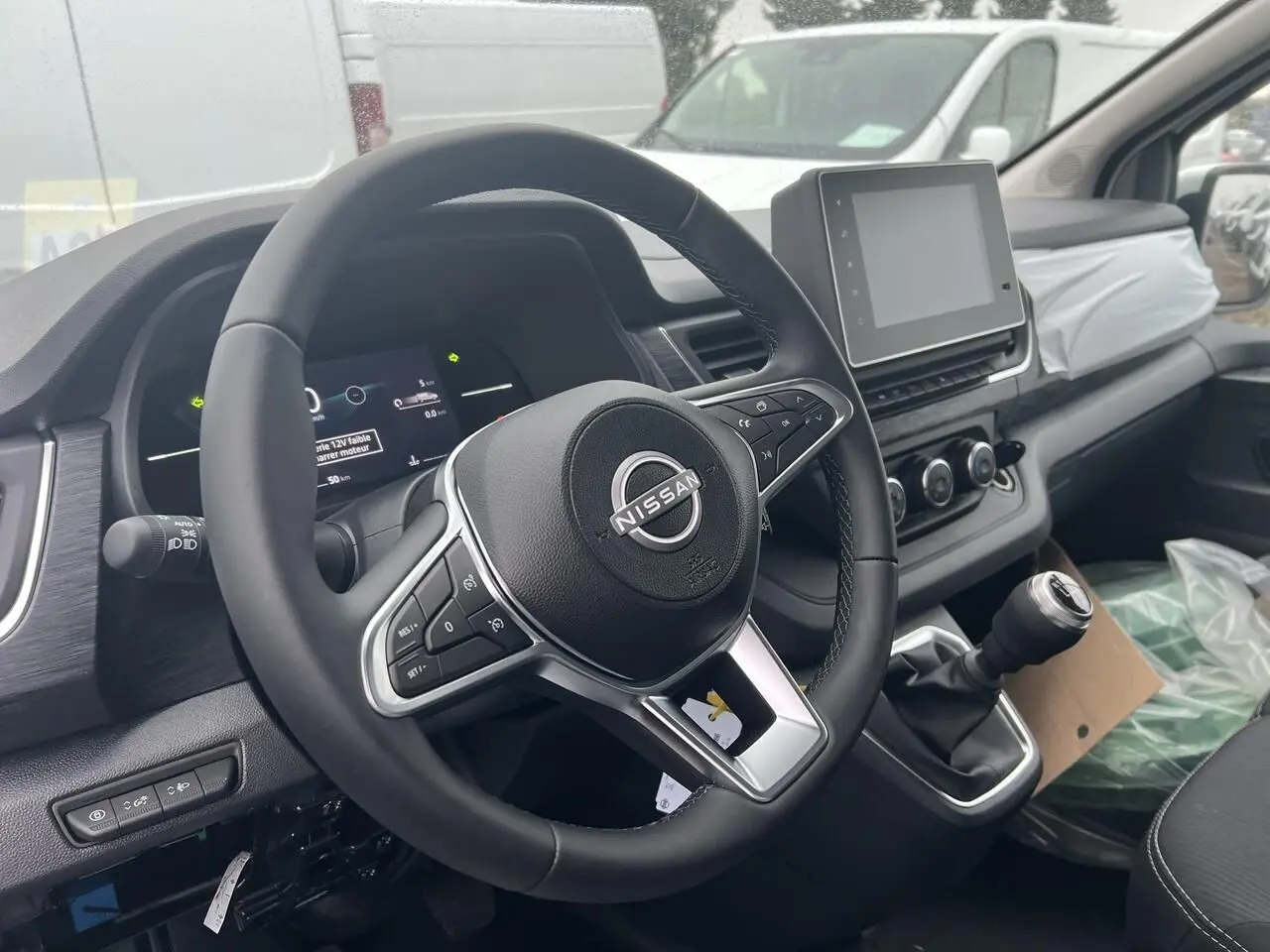 Vue intérieure côté conducteur du Nissan Primastar blanc 2025, volant multifonction et écran tactile central visible.