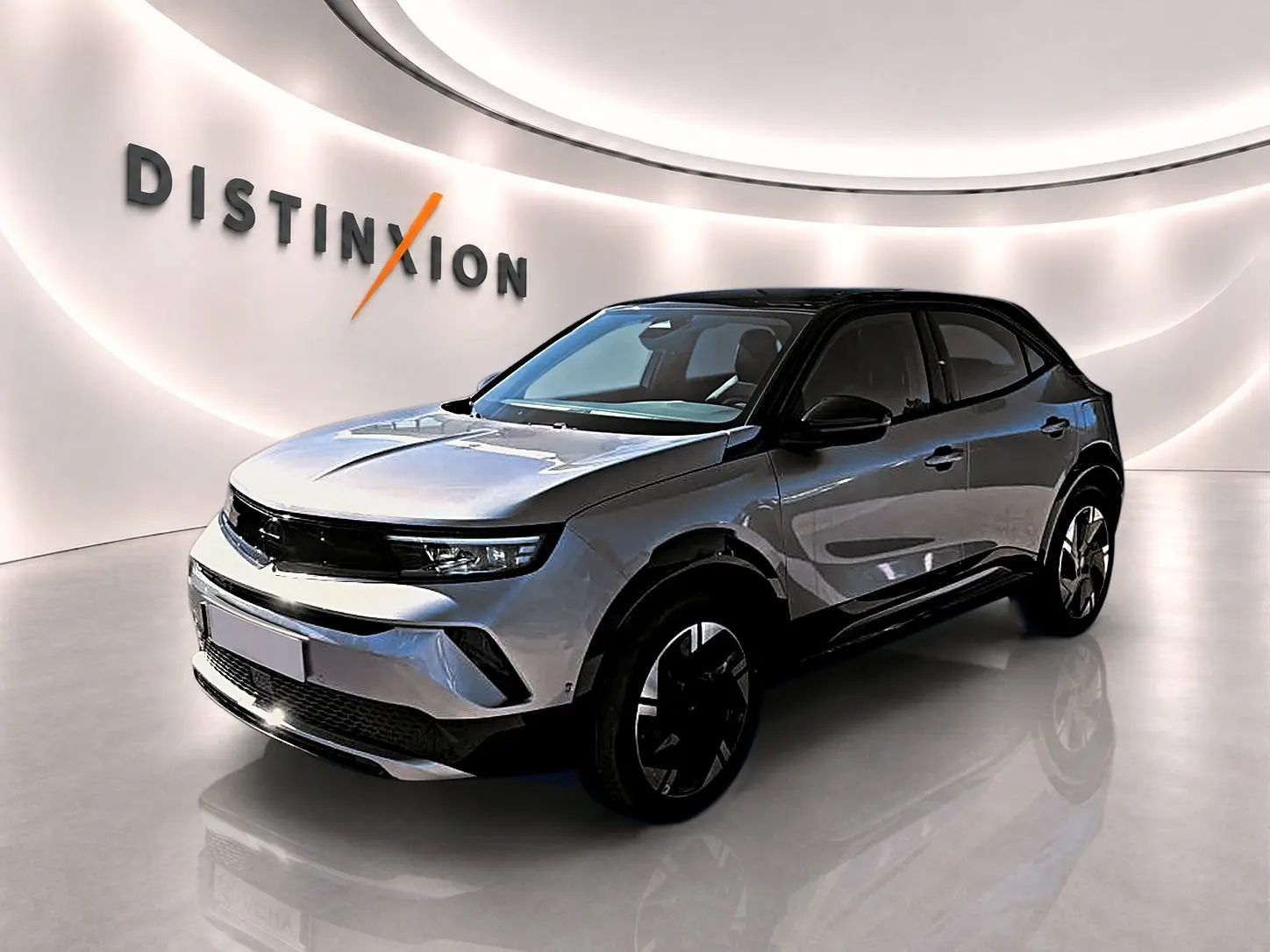 Opel Mokka Electric gris en 3/4 avant droit, toit noir et jantes alu distinctives dans un showroom lumineux.