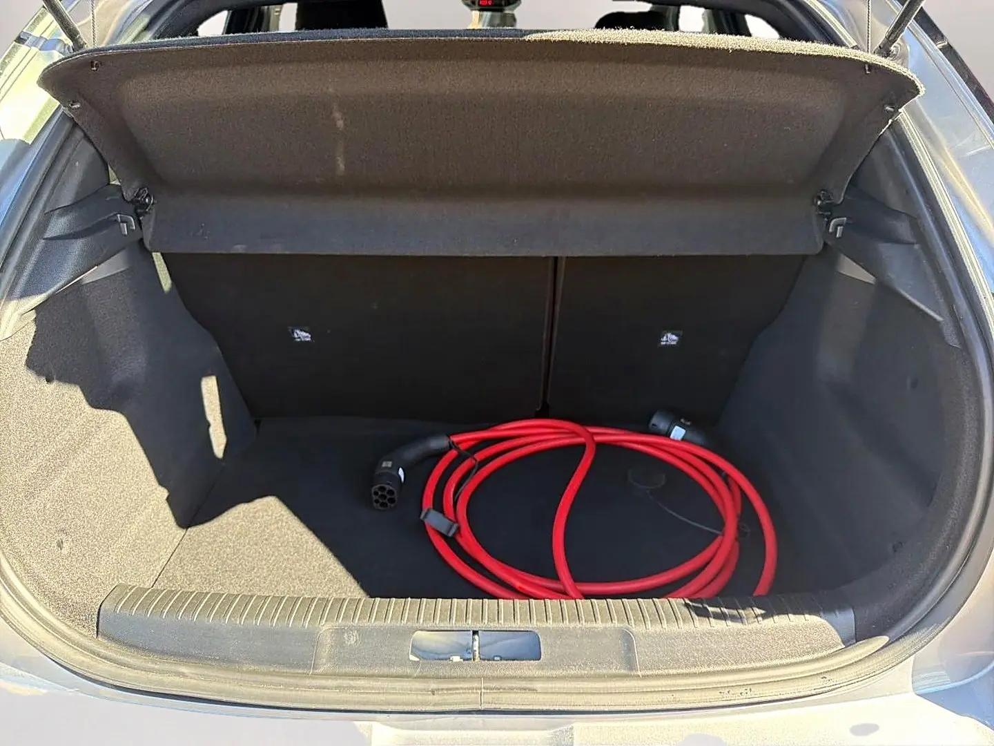 Coffre ouvert d’un Opel Mokka Electric gris, montrant un câble de recharge électrique rouge enroulé.