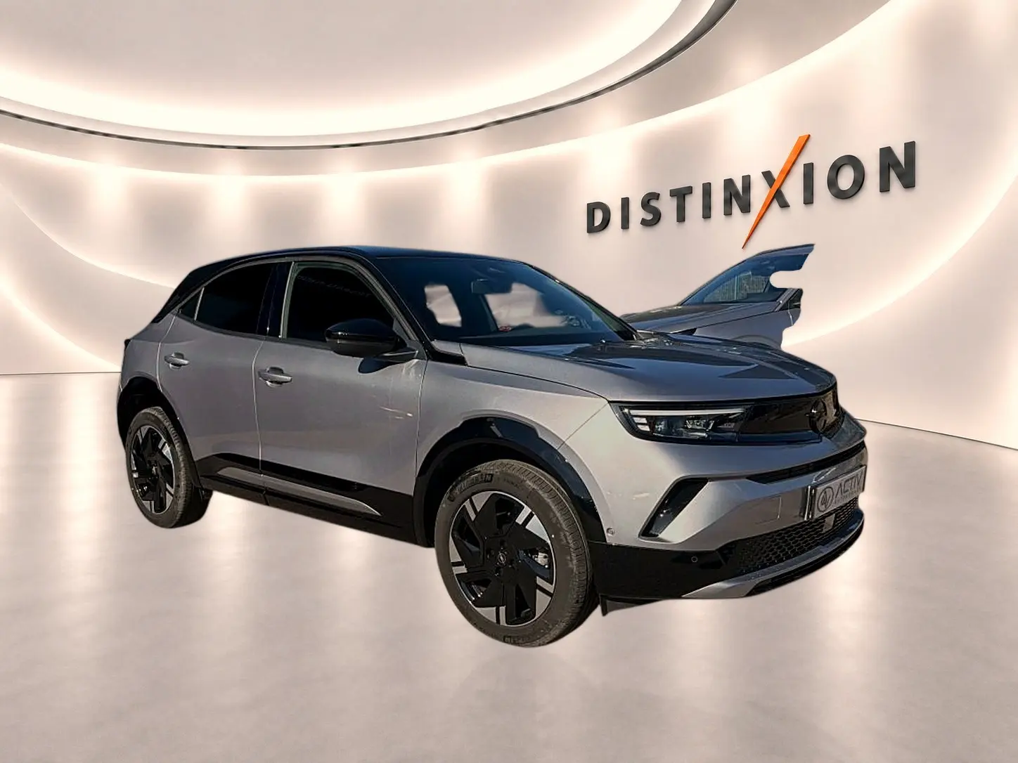 Opel Mokka Electric gris en 3/4 avant droit, avec jantes noires et toit noir dans un showroom lumineux.