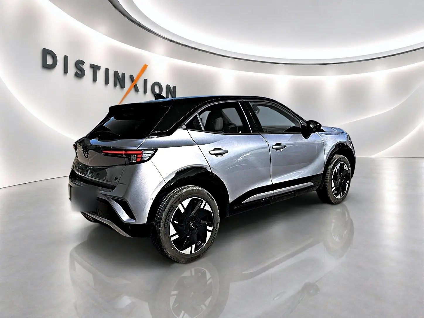 Opel Mokka Electric gris en 3/4 arrière droit, toit noir et jantes alu distinctives dans un showroom lumineux.