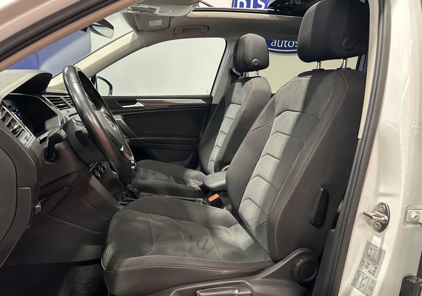 Vue intérieure côté conducteur du Volkswagen Tiguan Allspace blanc, sièges avant en tissu gris foncé et volant cuir.