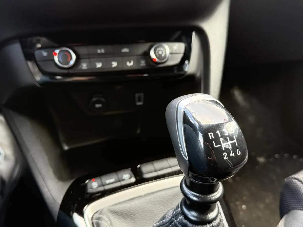 Le levier de vitesses manuel noir de l'Opel Corsa 1.2i Turbo 100 GS en gros plan avec console centrale en arrière-plan.