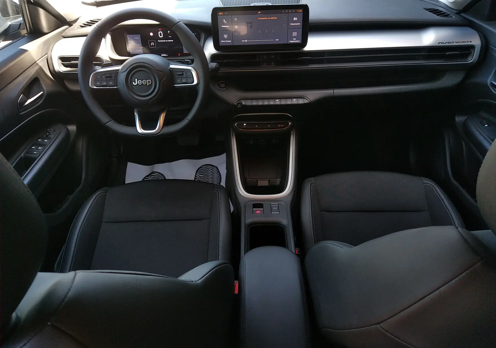 Vue intérieure avant du Jeep Avenger eHYBRID 2025, tableau de bord gris avec écran tactile et volant multifonction noir.