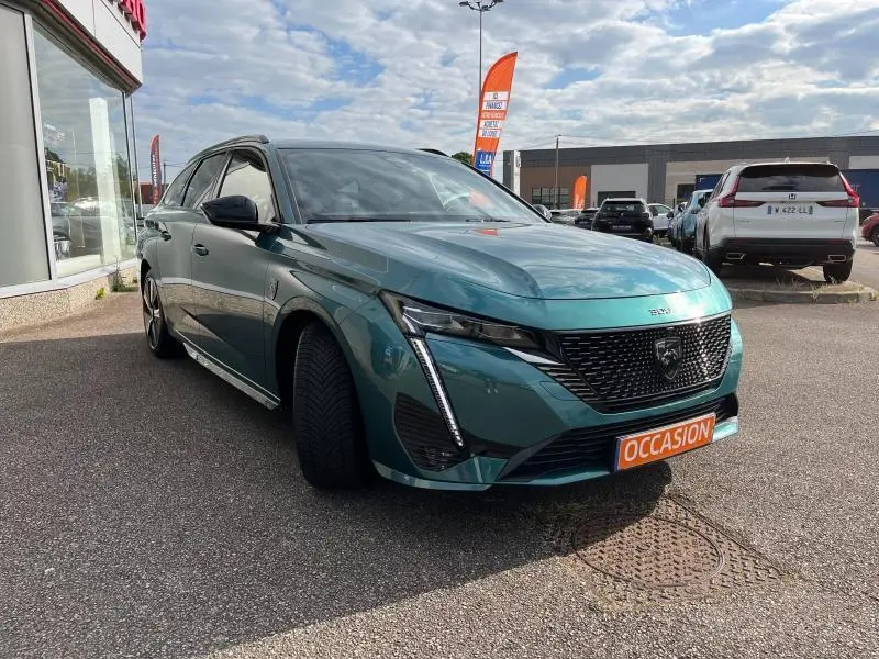 Peugeot 308 SW Bleu Avatar vue 3/4 avant droit, calandre noire et feux LED, stationnée devant un concessionnaire.