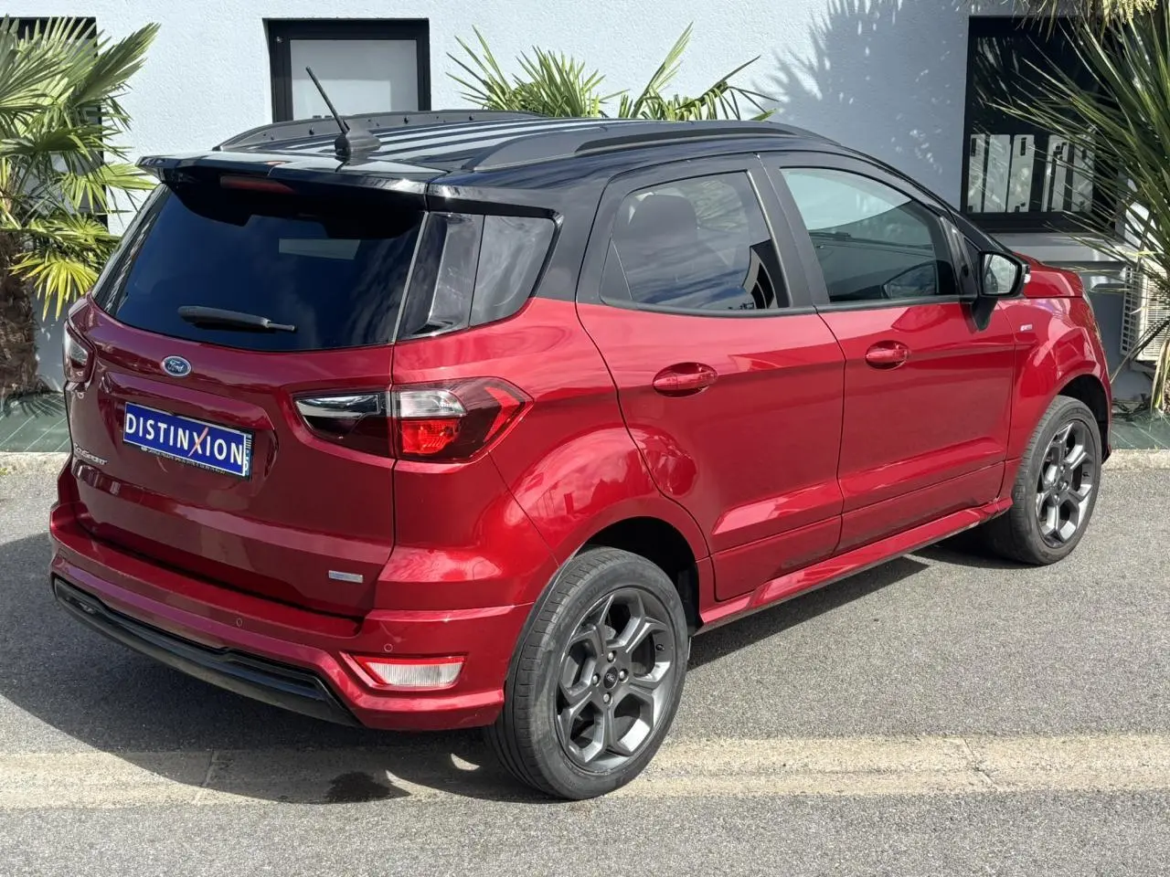 Vue 3/4 arrière droite du Ford EcoSport rouge métallisé avec toit noir et vitres arrière surteintées.