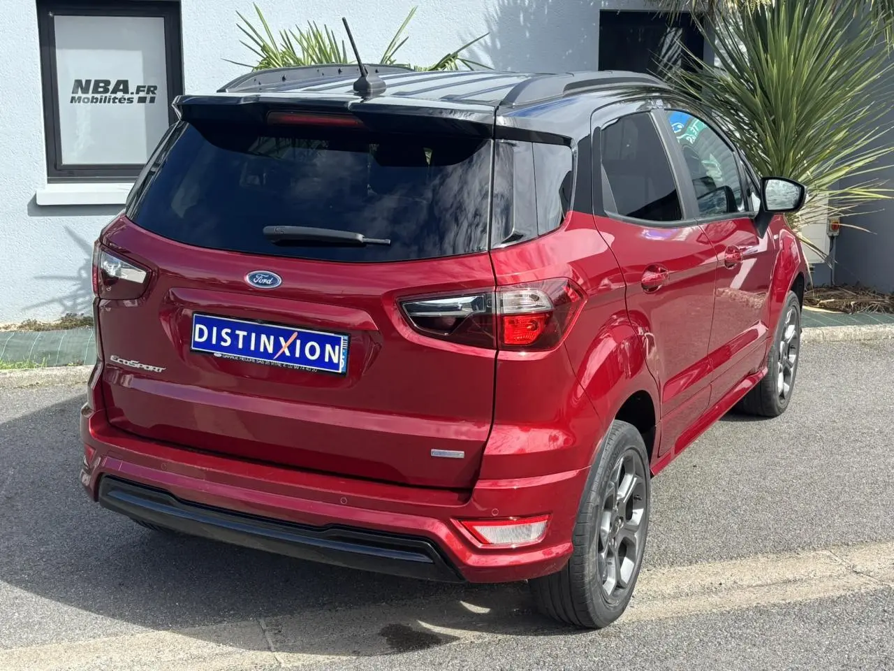 Vue 3/4 arrière droite d'un Ford EcoSport rouge métallisé avec vitres arrière surteintées et barres de toit noires.