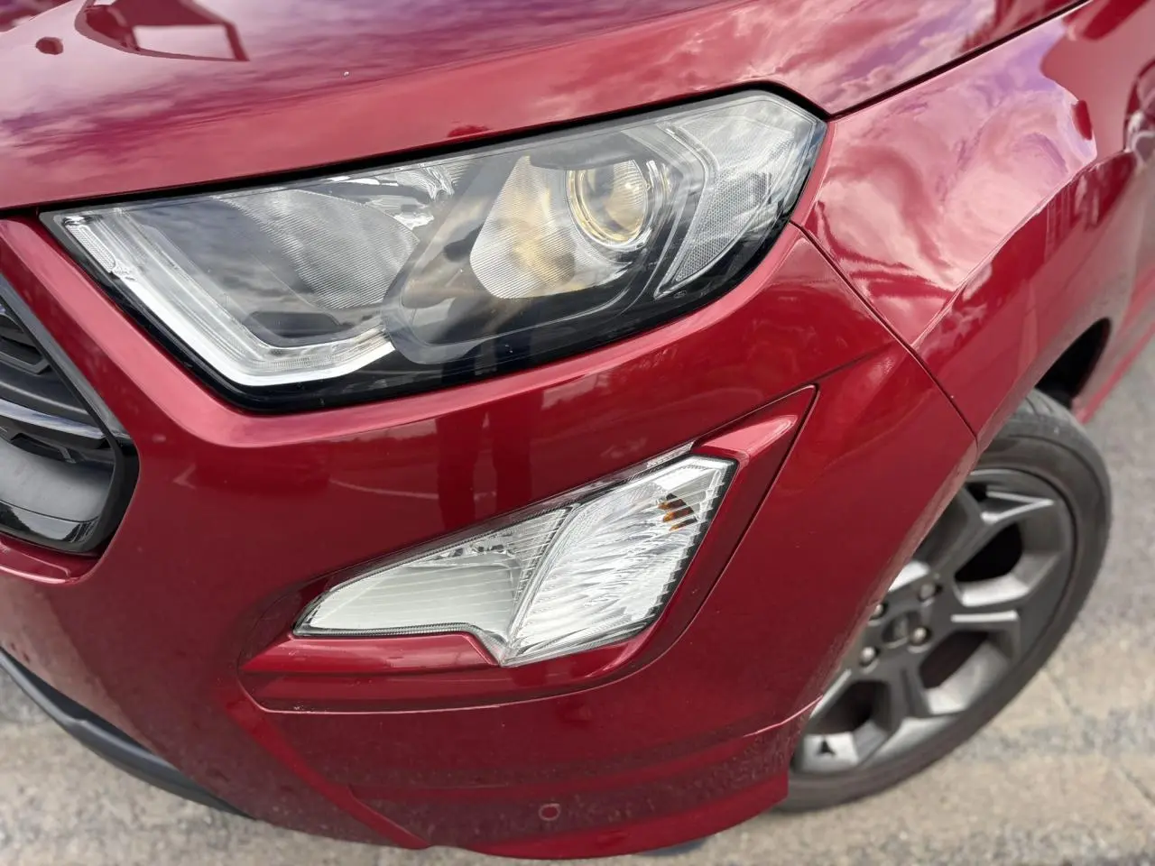 Gros plan sur le phare avant droit et la roue alliage 17 pouces du Ford EcoSport rouge métallisé.