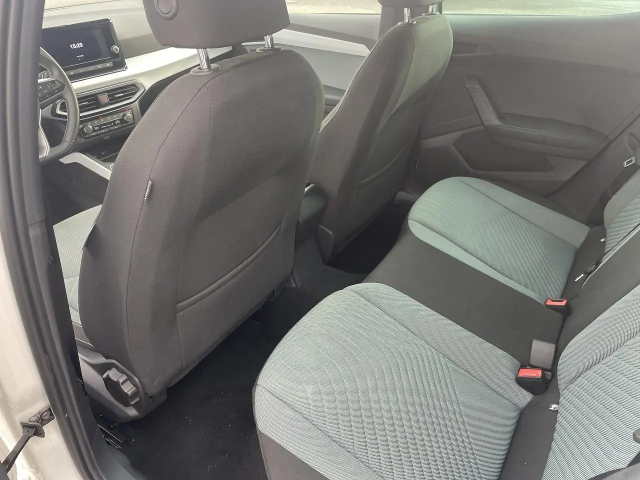 Vue intérieure arrière gauche de la SEAT IBIZA blanche 2025, sièges tissu bicolore et tableau de bord digital visible.