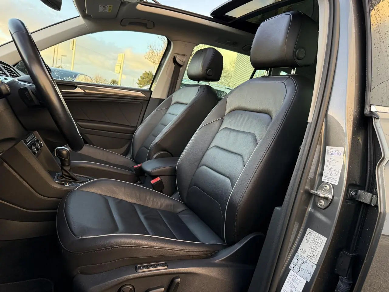 Vue intérieure côté gauche du Volkswagen Tiguan 2019, sièges sport cuir noir et toit ouvrant panoramique visibles.