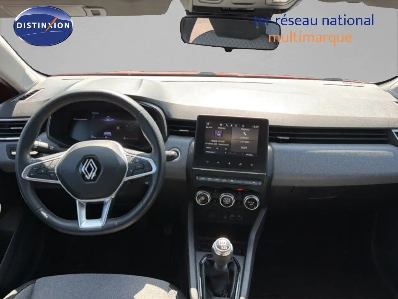 Vue intérieure avant de la Renault Clio V rouge flamme, tableau de bord moderne avec écran tactile et volant multifonction.