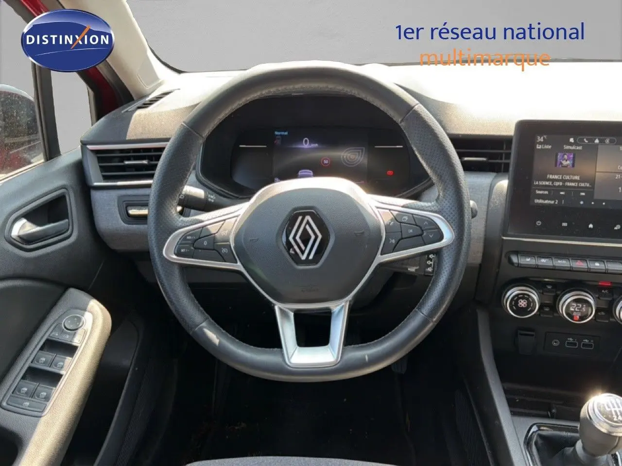 Vue intérieure centrée sur le volant Renault Clio V rouge flamme, avec tableau de bord digital et console tactile visible.