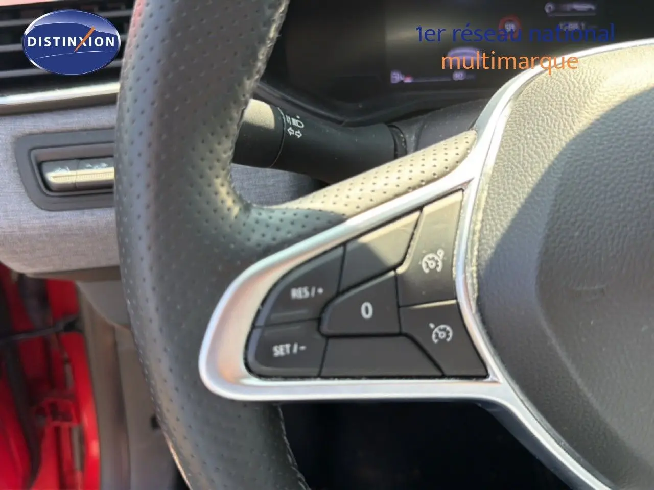 Gros plan sur les commandes au volant côté gauche de la Renault Clio V rouge flamme, avec boutons de régulateur de vitesse.