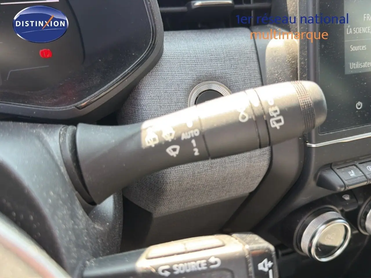 Gros plan sur la commande des essuie-glaces à gauche du volant dans l'habitacle d'une Renault Clio V rouge flamme.
