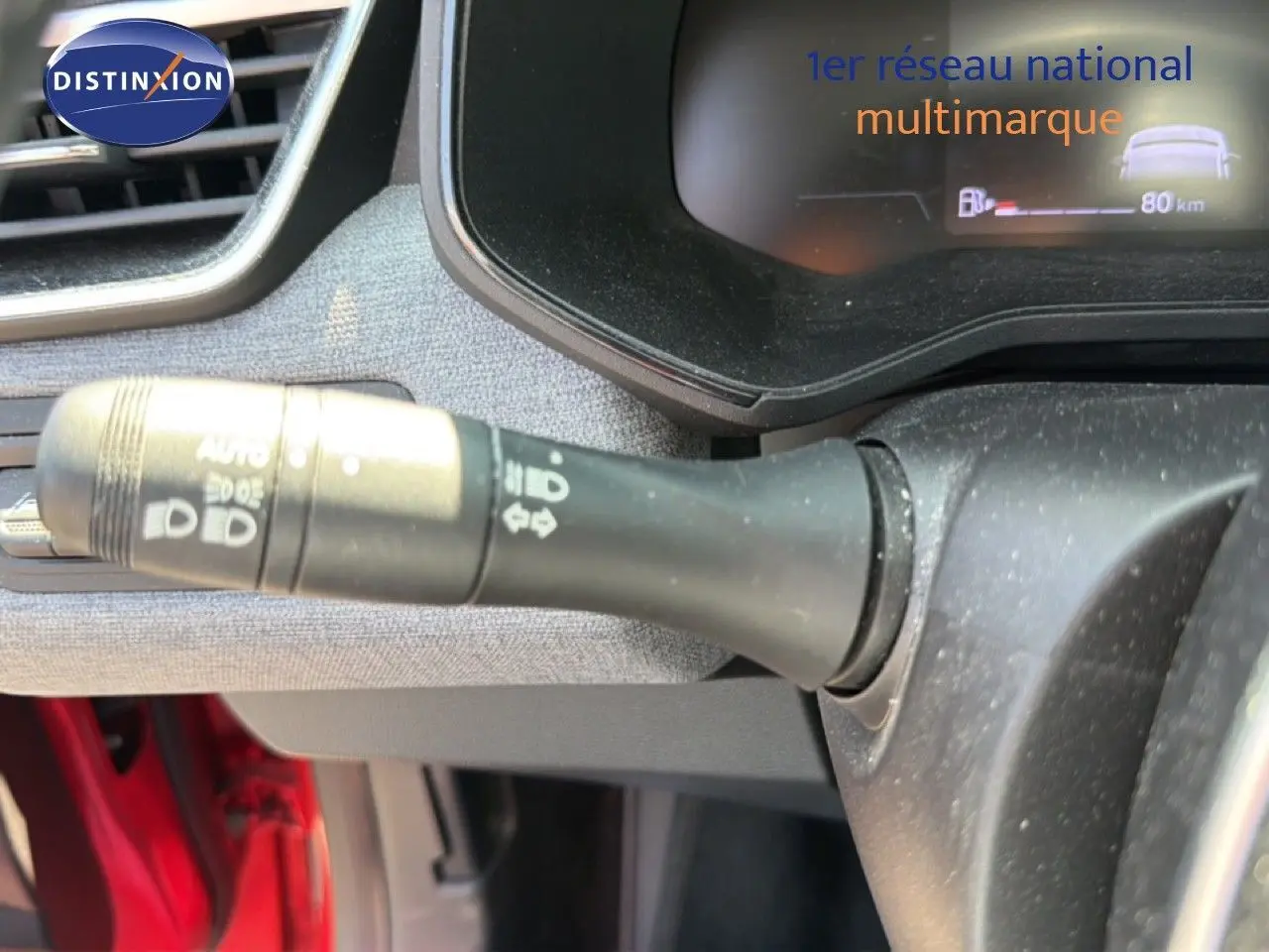 Gros plan sur la commande des phares à gauche du volant dans l’habitacle rouge flamme d’une Renault Clio V Evolution TCe 90.