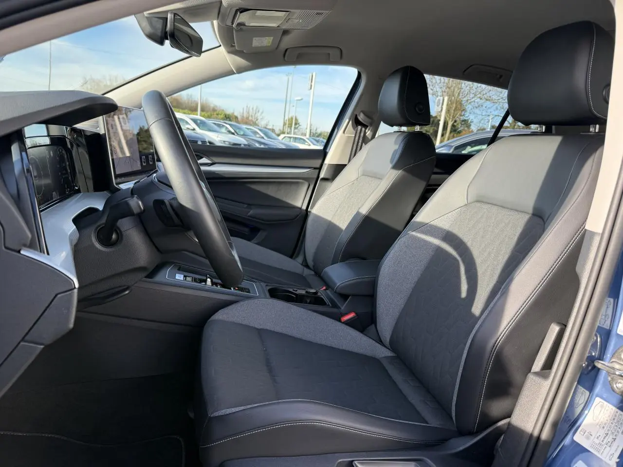 Vue intérieure côté conducteur de la Volkswagen Golf 2025 bleu anémone, avec sièges tissu et cuir gris et volant multifonction.