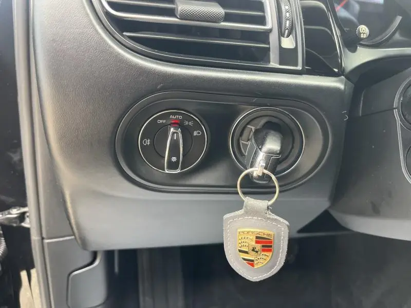 Gros plan sur la commande des phares et la clé avec porte-clés Porsche dans l'habitacle noir du Macan 2018.