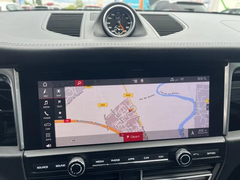 Vue rapprochée du tableau de bord noir du Porsche Macan 2018 avec écran tactile GPS et horloge centrale analogique.