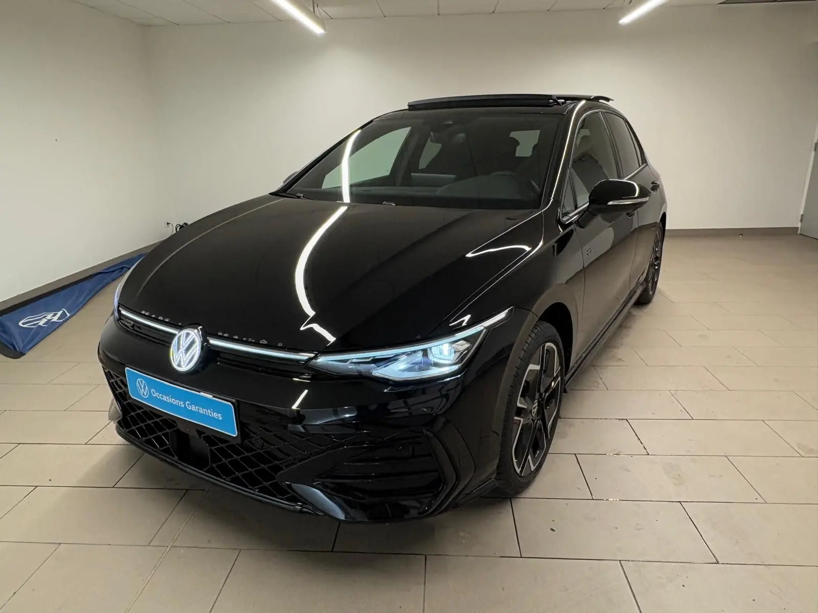 Vue 3/4 avant d'une Volkswagen Golf 2.0 TDI R-Line noire Grenadille avec phares allumés et toit ouvrant panoramique.