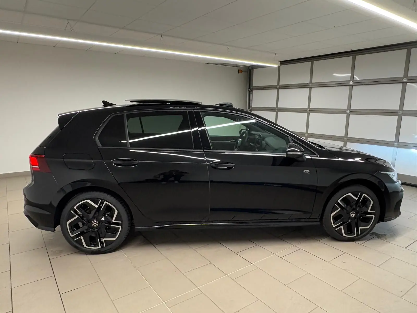 Volkswagen Golf 2.0 TDI R-Line noir grenadille vue de profil côté gauche en intérieur, toit ouvrant partiellement ouvert.