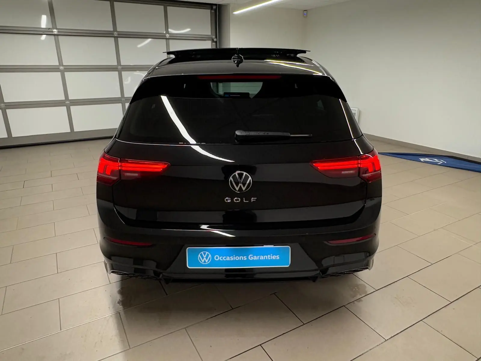 Vue arrière d'une Volkswagen Golf 2.0 TDI noire Grenadille avec feux allumés dans un garage fermé.