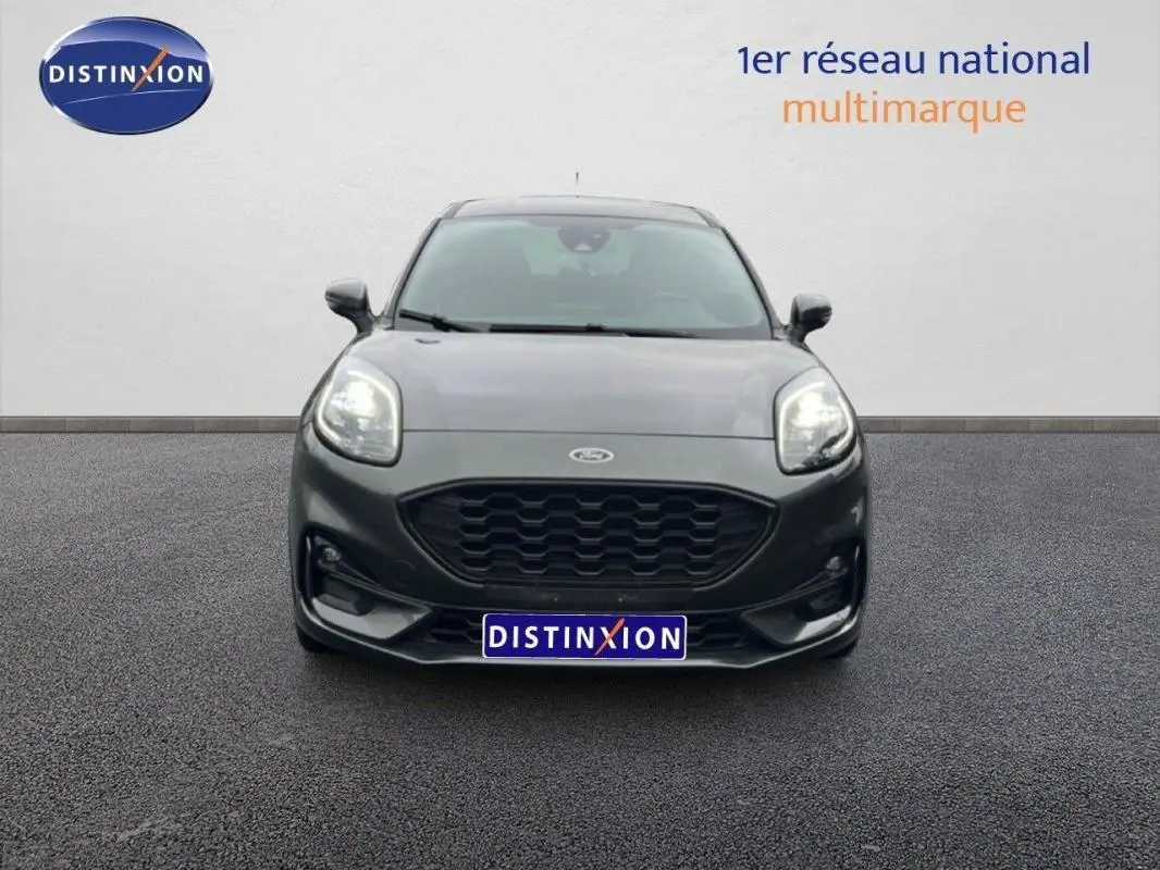 Vue avant d'un Ford Puma gris foncé 2024 avec calandre noire et phares allumés sur sol bitumé.