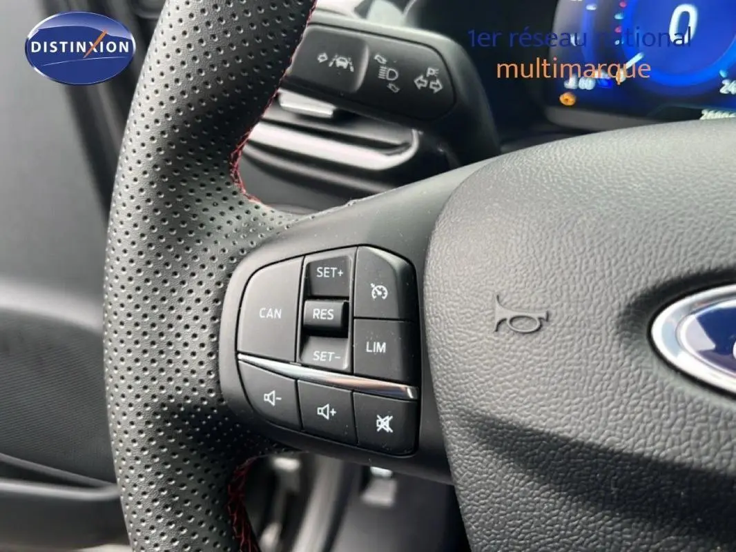 Gros plan sur le volant perforé gris foncé du Ford Puma 2024 avec commandes de régulateur et volume audio.