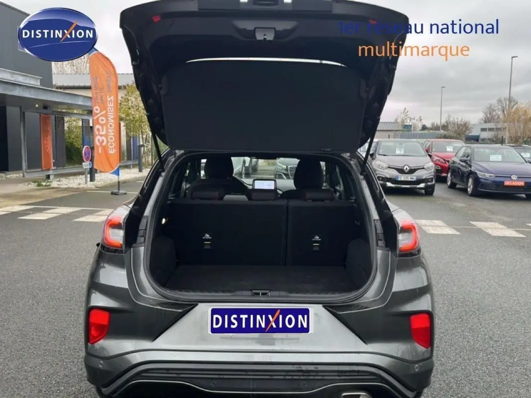 Vue arrière d'un Ford Puma gris foncé 2024 avec coffre ouvert, feux arrière allumés et jantes alliage 17 pouces visibles.