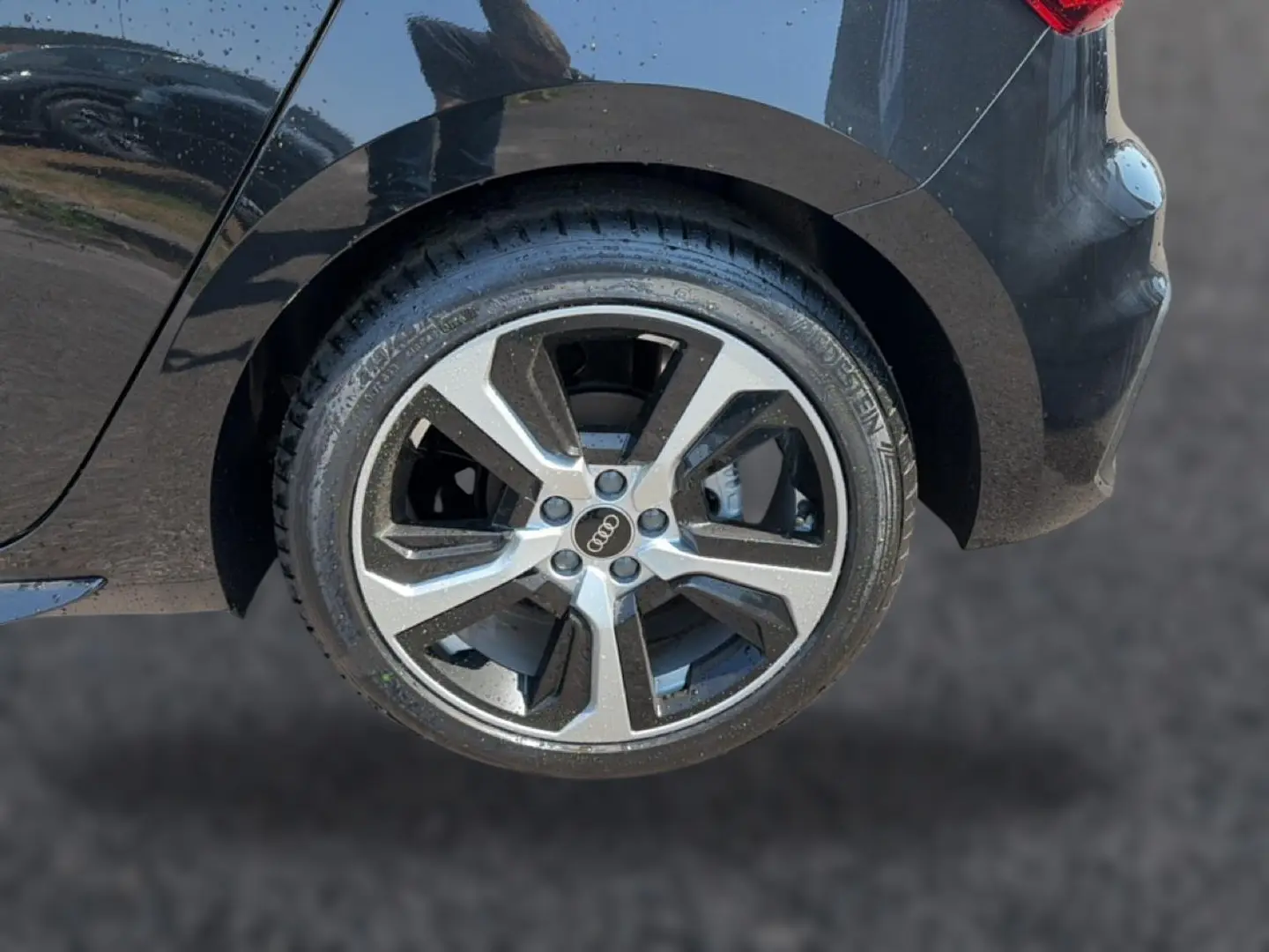 Gros plan sur la roue arrière droite d'une Audi A1 Sportback noire, mettant en valeur la jante alu au design moderne.