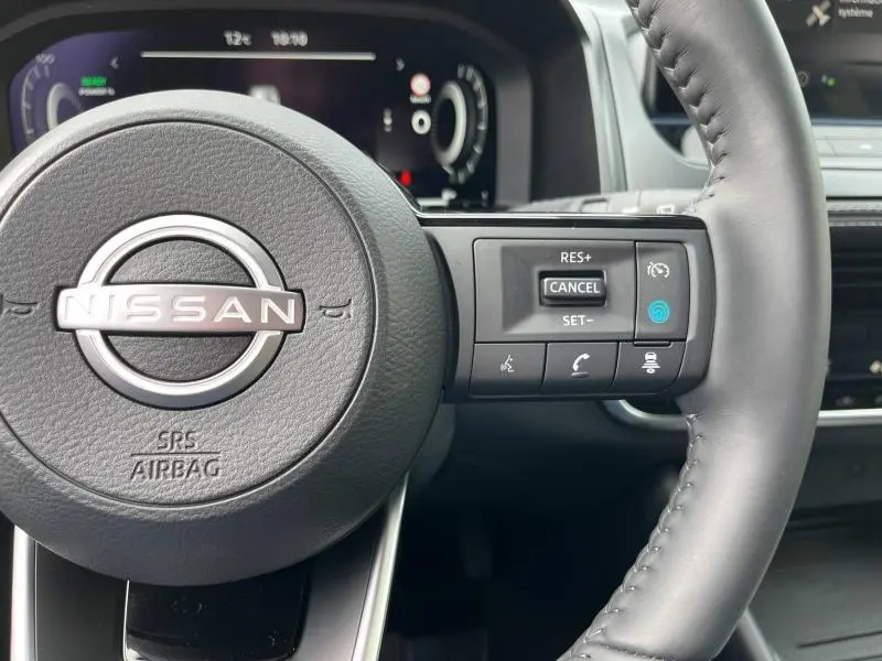Gros plan sur le volant cuir noir du Nissan Qashqai e-POWER 2024 avec commandes multifonctions à droite et tableau de bord digital.
