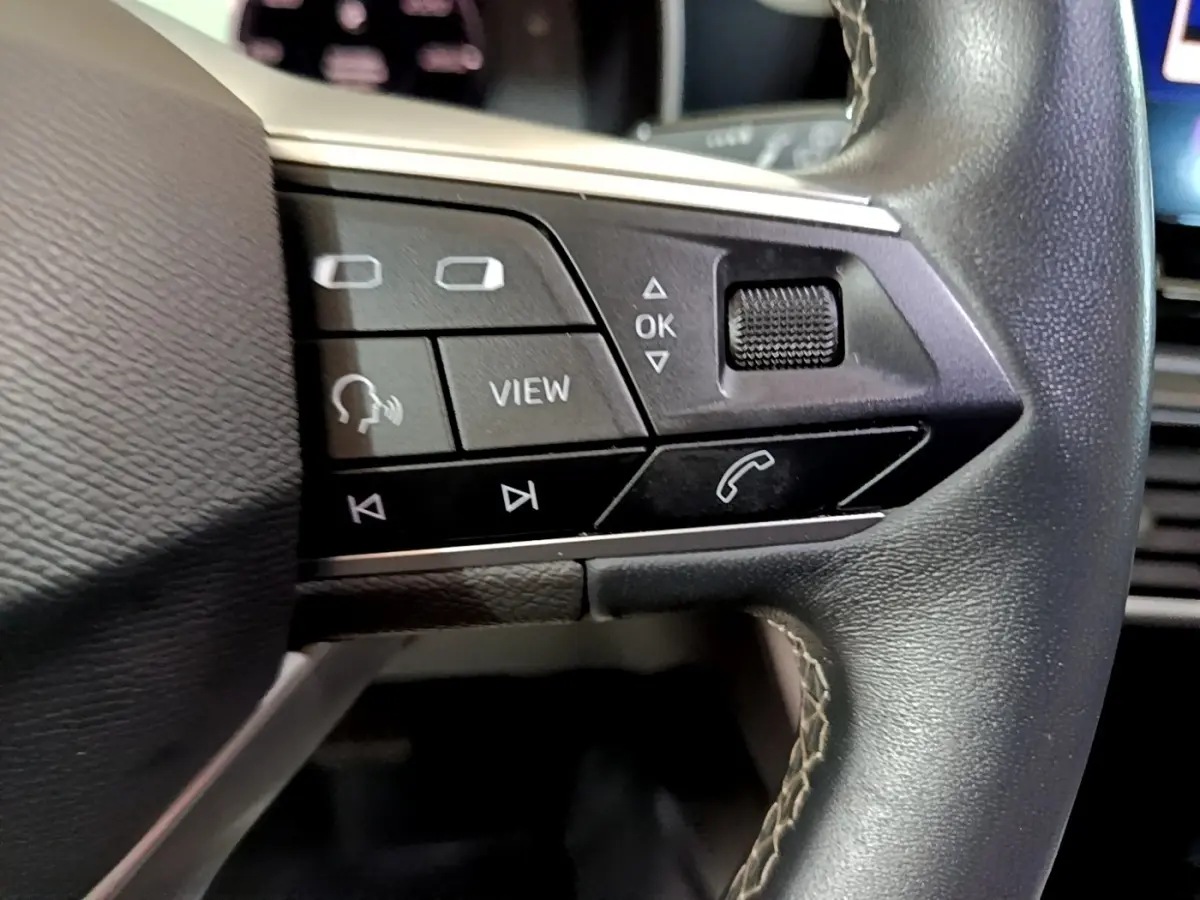 Gros plan sur les commandes gauche du volant cuir du SEAT LEON gris clair 2022, avec boutons multifonctions et molette.