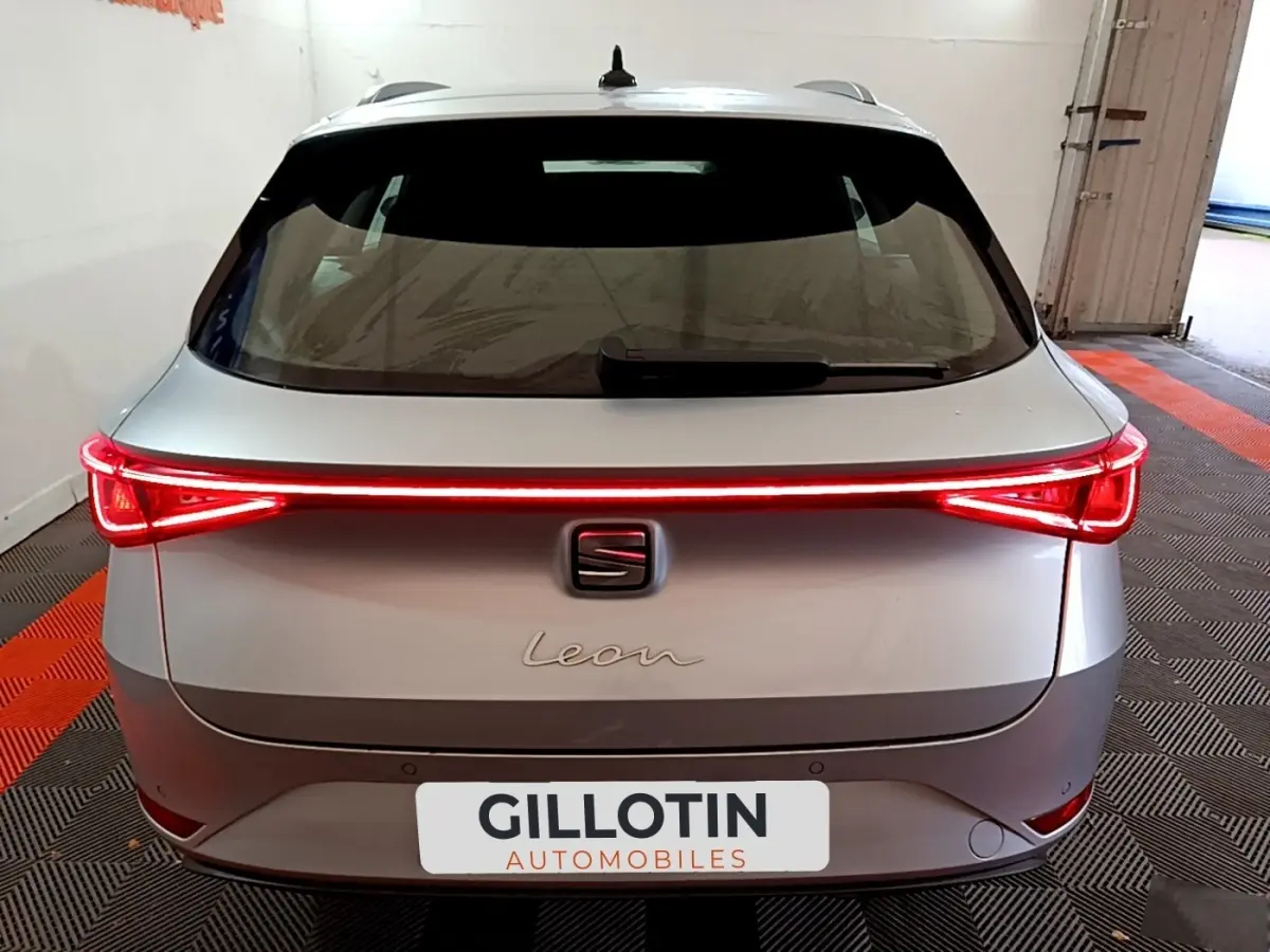 Vue arrière d'une SEAT Leon gris clair 2022 avec feux arrière LED allumés et logo central visible.