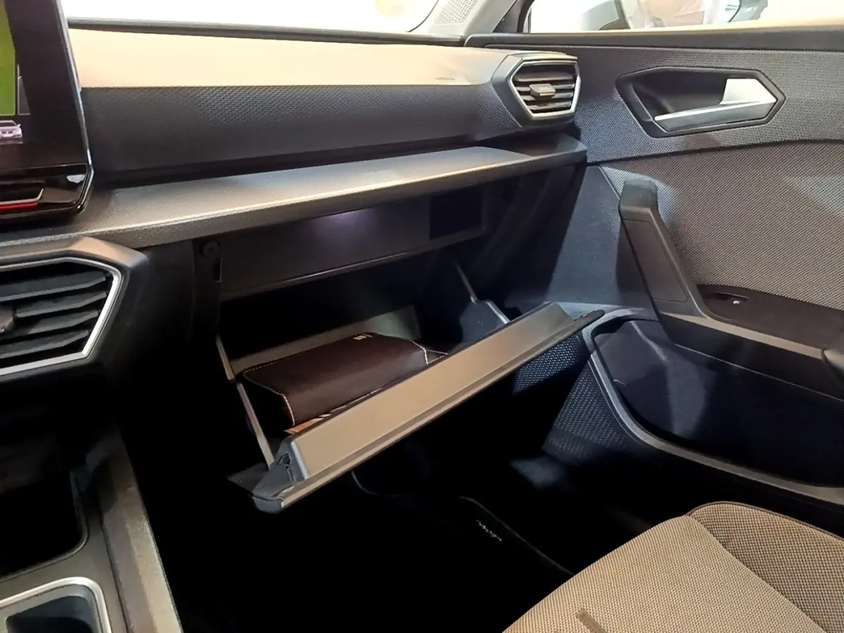 Vue intérieure côté passager du tableau de bord gris foncé avec boîte à gants ouverte et siège tissu clair d'une SEAT Leon 2022.