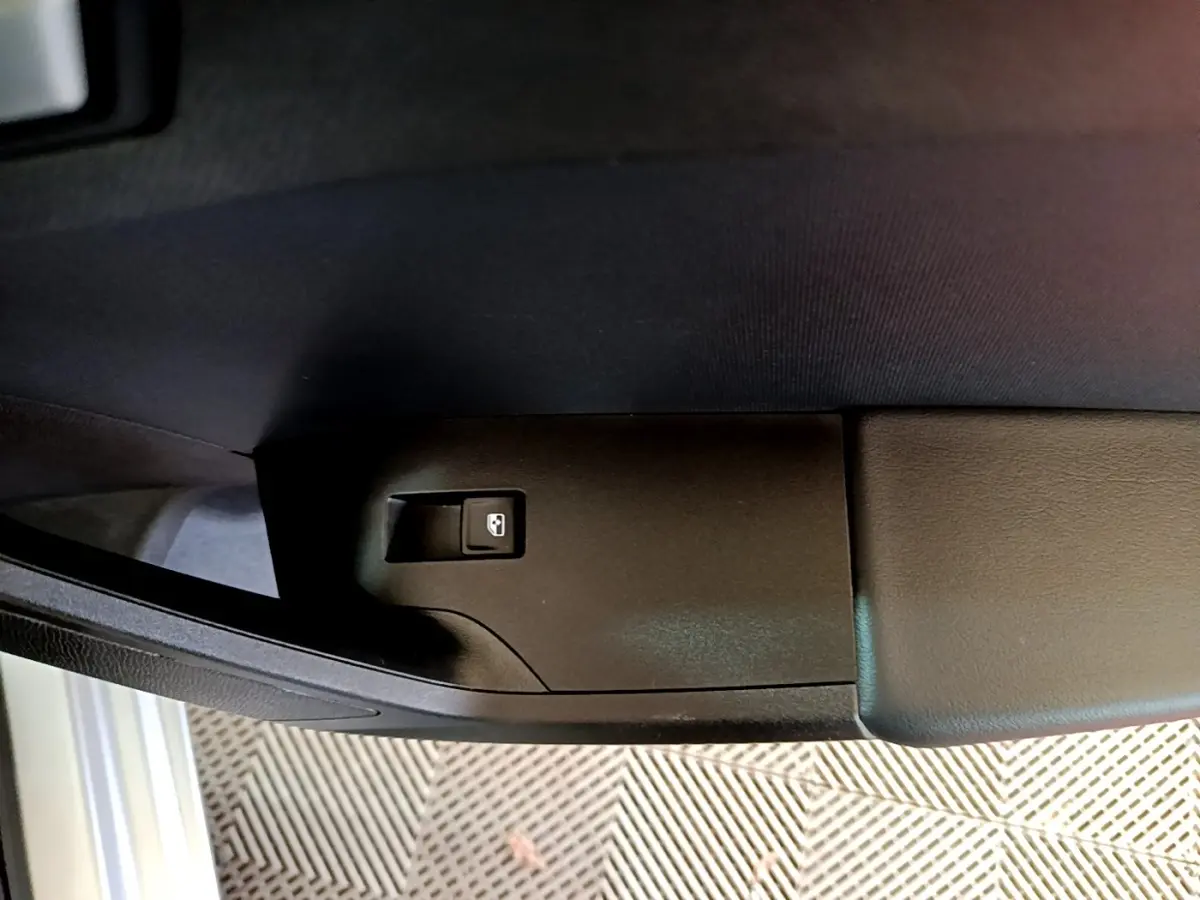 Bouton de commande de lève-vitre arrière droit noir sur panneau de porte intérieur gris foncé d'une SEAT Leon 2022.