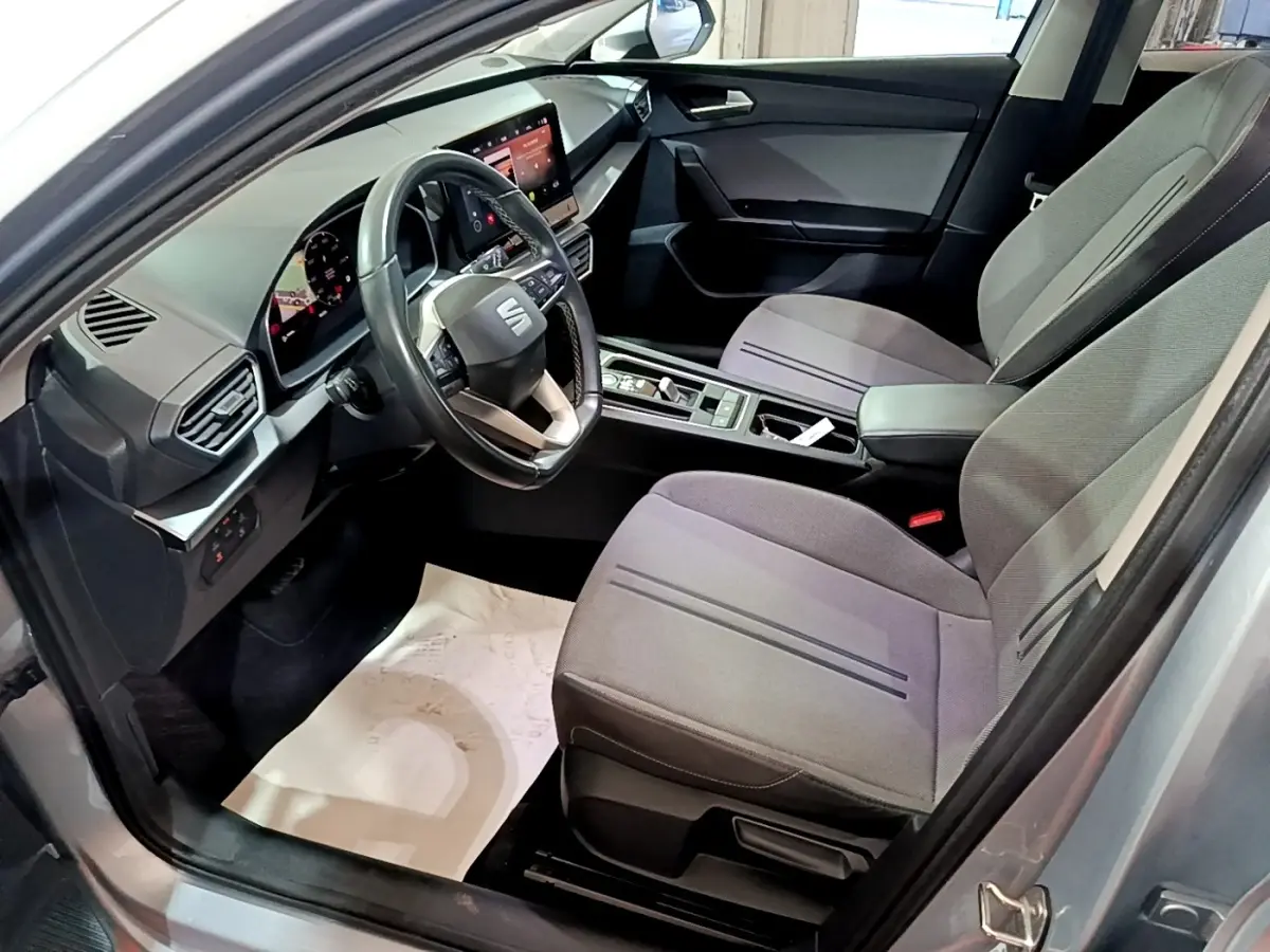 Intérieur avant droit du SEAT LEON gris clair 2022, volant cuir, écran tactile et sièges tissu gris.