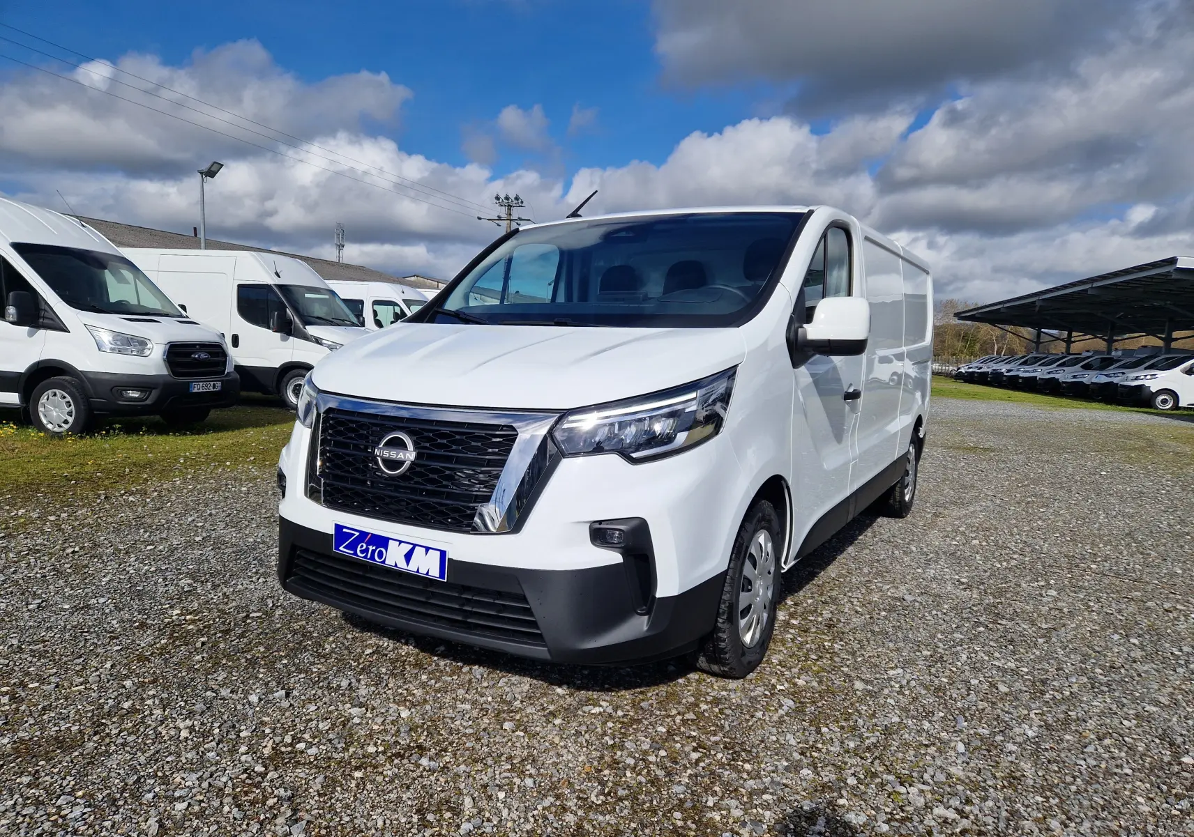 Vue 3/4 avant droite d’un utilitaire Nissan Primastar blanc avec calandre noire et plaque Zero KM sur un terrain extérieur.