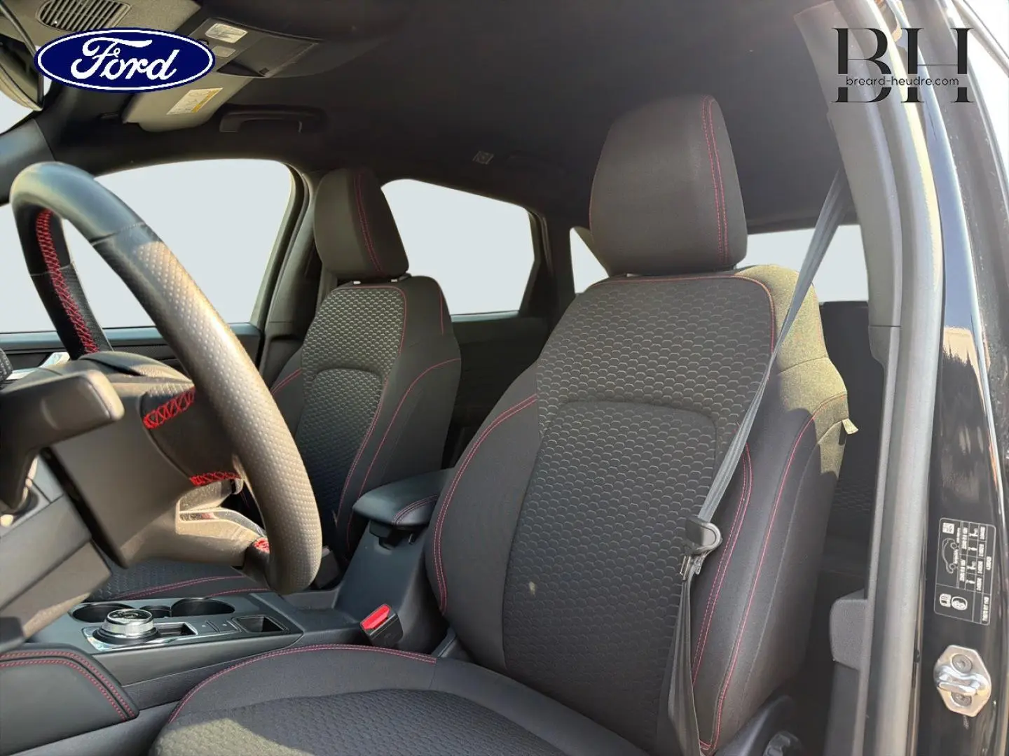 Vue intérieure avant droite du Ford Kuga 2025 noir Agate, sièges tissu ST-Line avec surpiqûres rouges et volant multifonction.