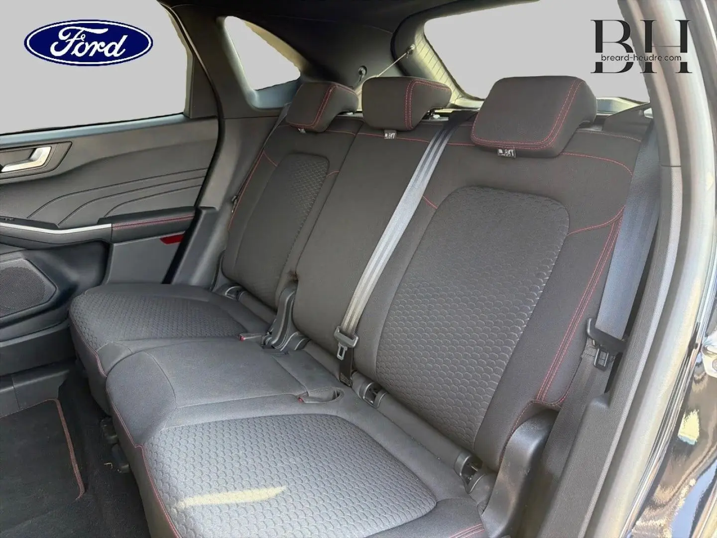 Vue intérieure du Ford Kuga 2025 montrant la banquette arrière en tissu noir avec surpiqûres rouges et ceintures grises.