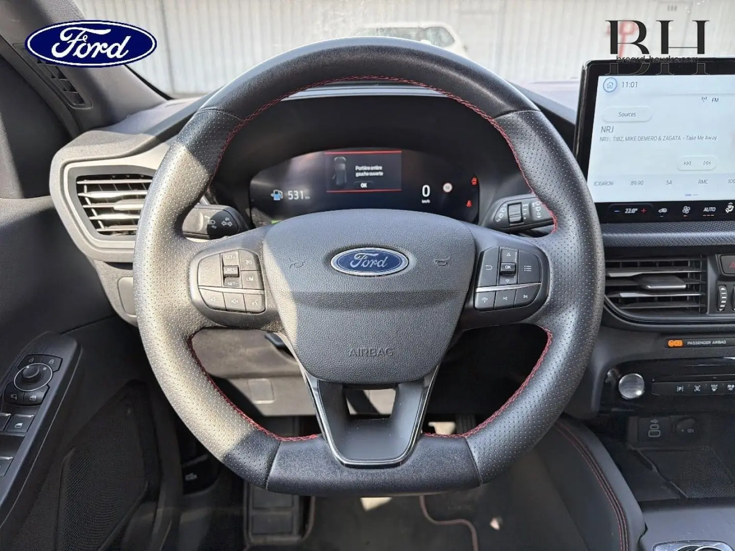 Vue rapprochée du volant en cuir noir avec surpiqûres rouges du Ford Kuga 2025, tableau de bord et écran tactile visibles.
