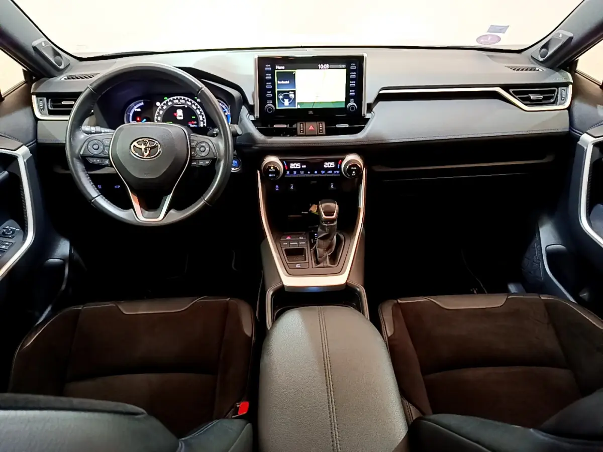 Vue intérieure frontale du tableau de bord et volant cuir noir du Toyota RAV4 gris clair avec écran tactile central et console moderne.