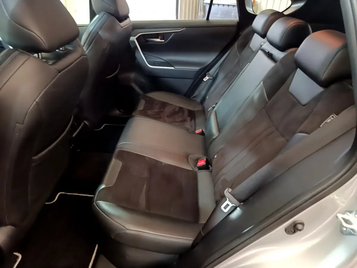 Vue intérieure arrière droite du Toyota RAV4 gris clair 2019, sièges en cuir noir avec inserts alcantara et ceintures de sécurité visibles.