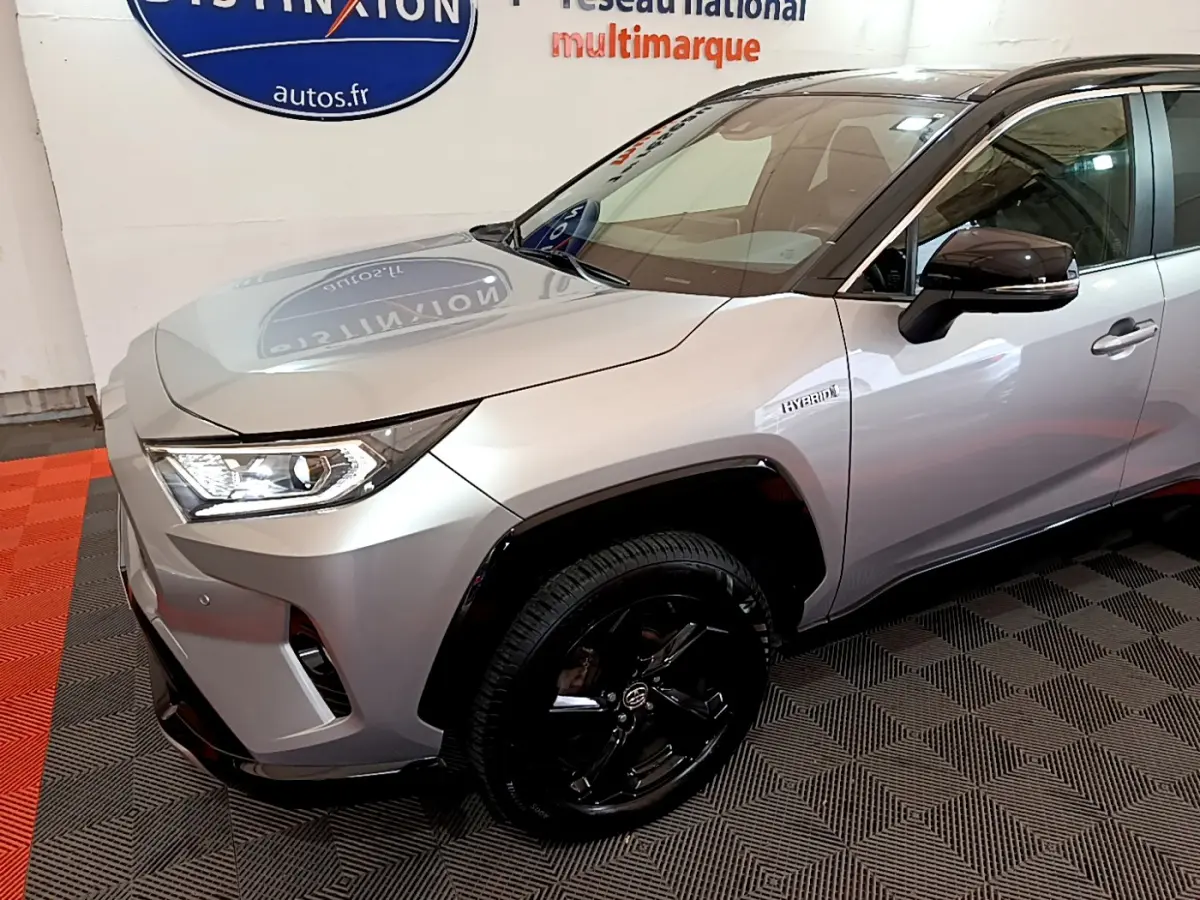 Vue 3/4 avant droit d'un Toyota RAV4 gris clair hybride avec jantes noires et badge Hybrid sur aile avant.