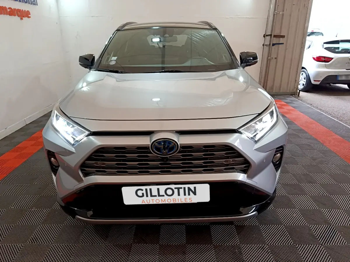 Vue frontale d'un Toyota RAV4 gris clair 2WD 218ch avec calandre noire et phares LED allumés dans un garage.