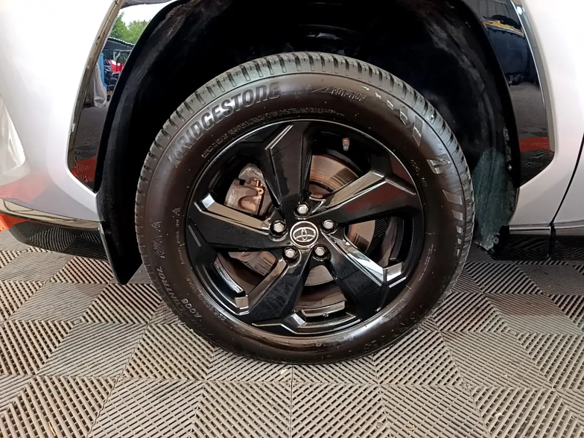 Gros plan sur la roue avant gauche du Toyota RAV4 gris clair, jante alliage noir brillant avec logo Toyota central.
