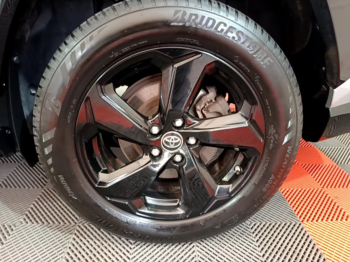 Gros plan sur la roue avant droite du Toyota RAV4 gris clair, jante noire brillante avec logo Toyota central.