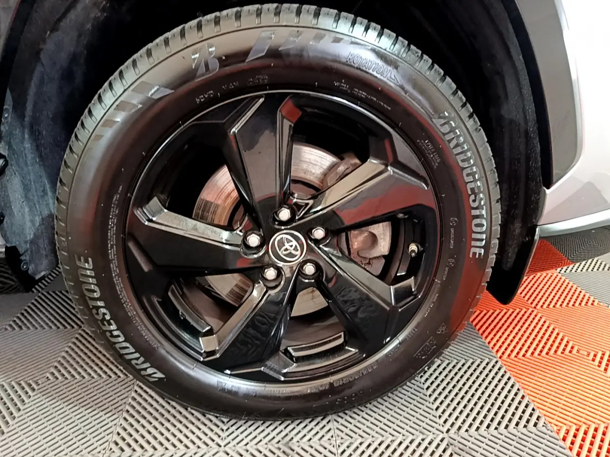 Gros plan sur la roue avant droite du Toyota RAV4 gris clair, jante noire brillante avec logo Toyota central.