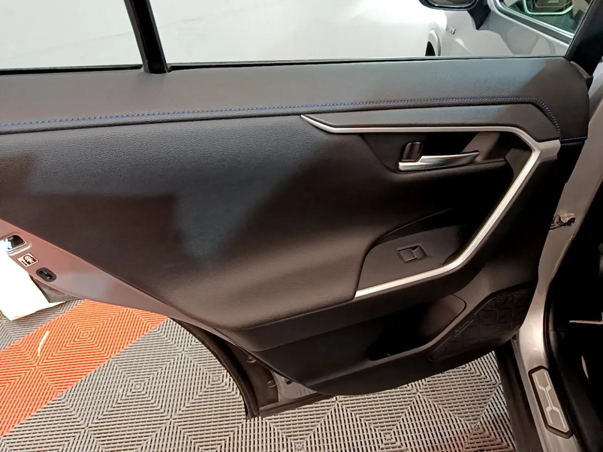 Porte arrière droite ouverte d’un Toyota RAV4 gris clair, montrant le panneau intérieur noir avec insert argenté.