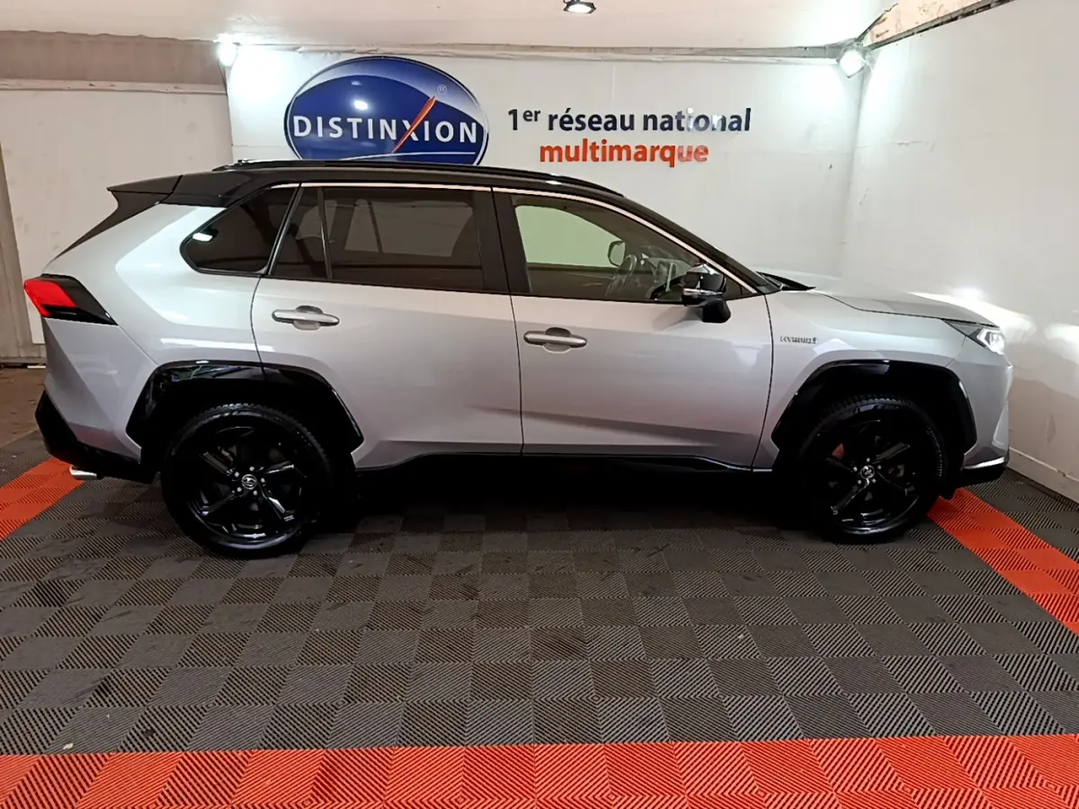 Profil côté droit d'un Toyota RAV4 gris clair 2WD 218ch Collection avec jantes noires et toit noir en showroom.